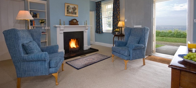 Photo of armchairs and fireplace with coastal view in The Captain's Quarter.