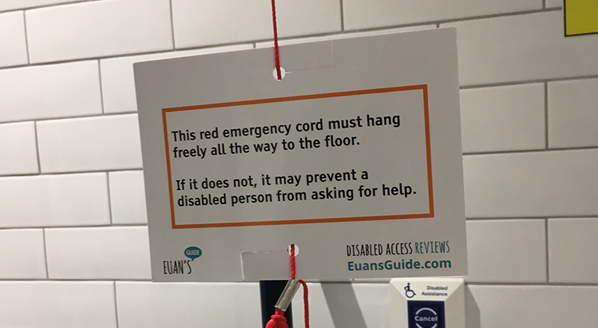 A Red Cord Card attached to a red emergency cord against a white tiled background. Text on the card reads: "This red emergency cord must hang freely all the way to the floor. If it does not, it may prevent a disabled person from asking for help."